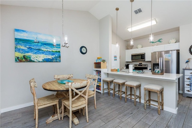 kitchen featuring a breakfast bar area, light wood finished floors, stainless steel appliances, visible vents, and a peninsula