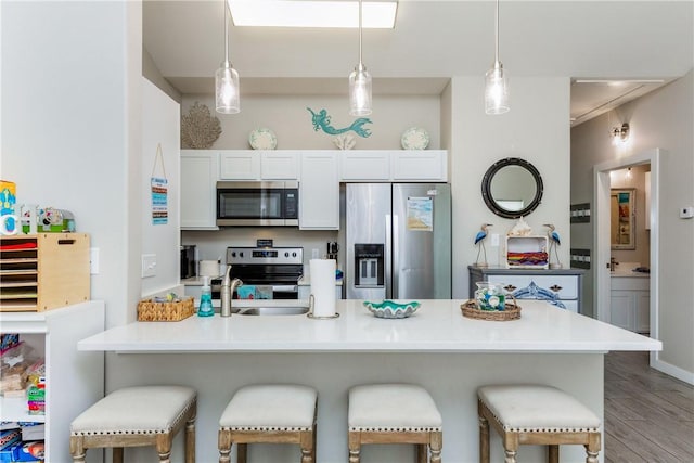 kitchen featuring decorative light fixtures, light wood finished floors, appliances with stainless steel finishes, a peninsula, and a kitchen breakfast bar