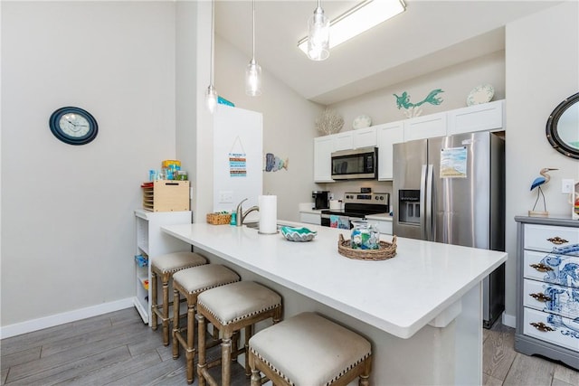 kitchen with light wood finished floors, white cabinets, appliances with stainless steel finishes, a breakfast bar area, and a peninsula