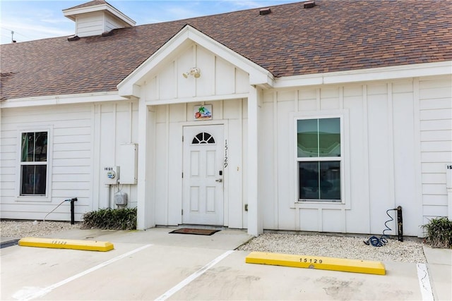 entrance to property with uncovered parking, roof with shingles, and board and batten siding