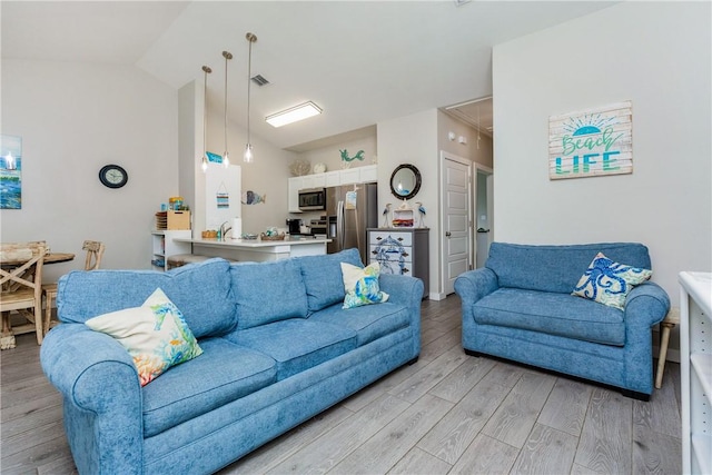 living area with lofted ceiling, light wood-style floors, attic access, and visible vents