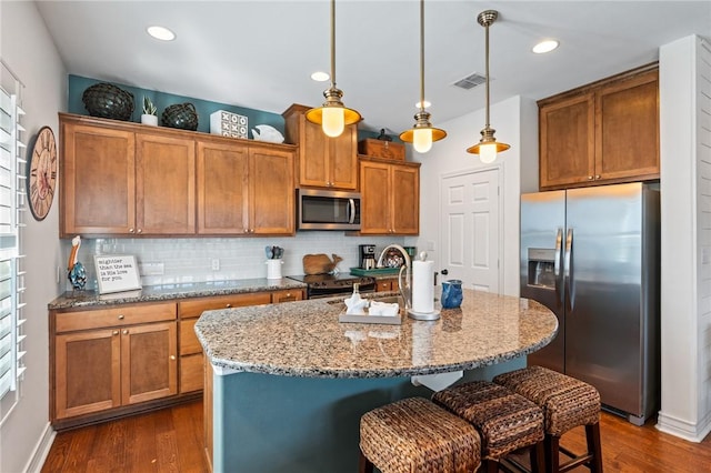 kitchen featuring hanging light fixtures, plenty of natural light, stainless steel appliances, and a kitchen island with sink