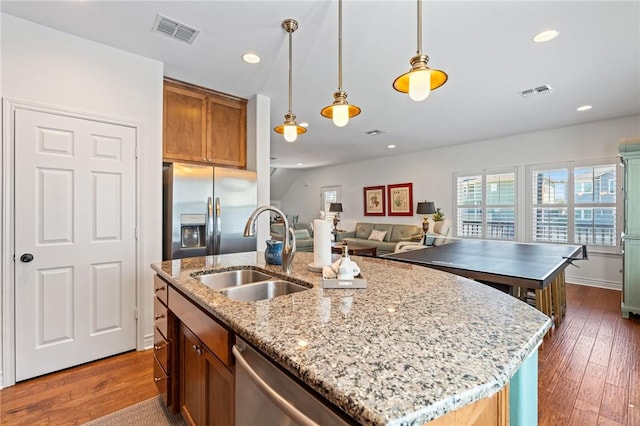 kitchen with a kitchen island with sink, sink, dark wood-type flooring, and appliances with stainless steel finishes