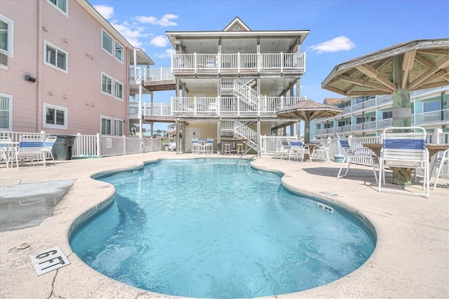 community pool with a patio area, stairway, and fence