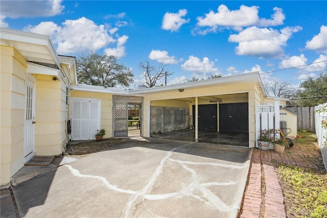 rear view of property with concrete driveway, a carport, and fence