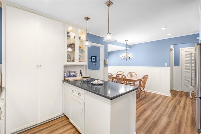 kitchen with a peninsula, light wood-style flooring, wainscoting, and white cabinetry