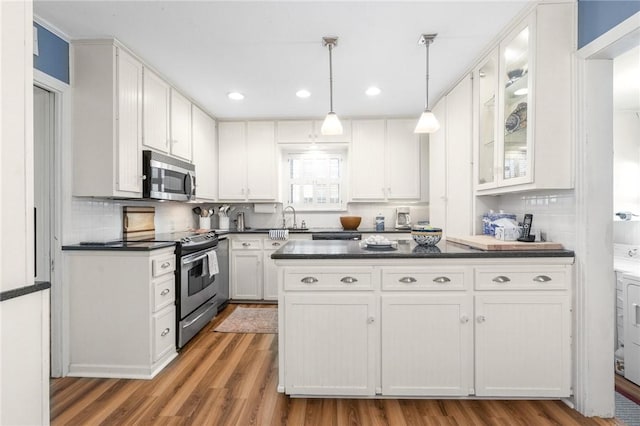 kitchen with appliances with stainless steel finishes, dark countertops, a sink, and white cabinets