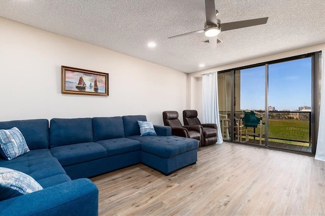 living room with ceiling fan, a textured ceiling, and light wood-type flooring