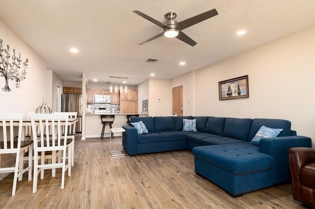 living room featuring light hardwood / wood-style flooring, ceiling fan, and a textured ceiling