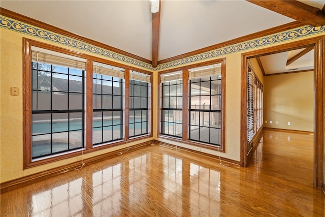 empty room featuring hardwood / wood-style floors, vaulted ceiling with beams, and crown molding