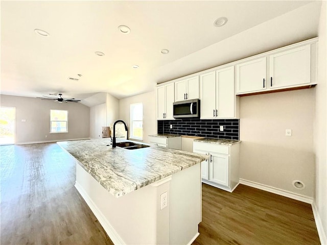 kitchen featuring lofted ceiling, stainless steel microwave, a sink, white cabinetry, and backsplash