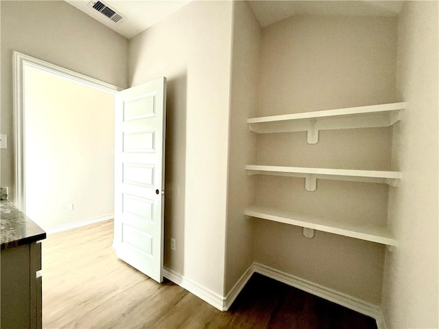 hall with baseboards, visible vents, and wood finished floors