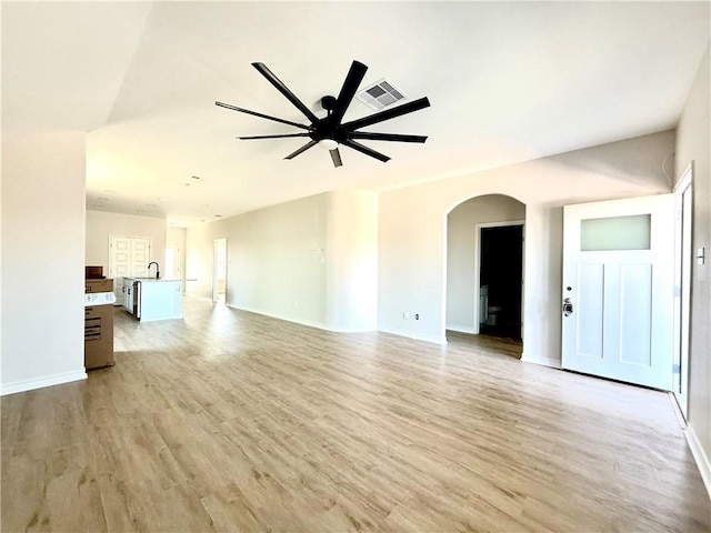 unfurnished living room with arched walkways, a ceiling fan, baseboards, visible vents, and light wood-style floors