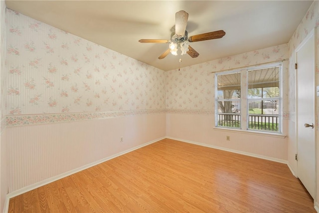 unfurnished room featuring wallpapered walls, ceiling fan, a wainscoted wall, light wood finished floors, and baseboards
