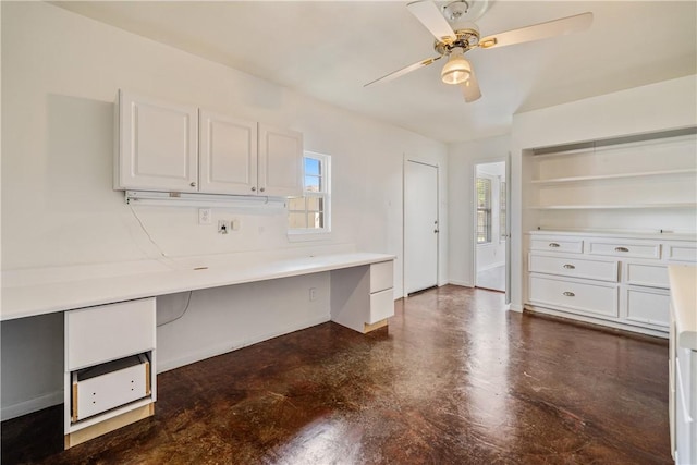 unfurnished office with baseboards, built in desk, a ceiling fan, and finished concrete flooring