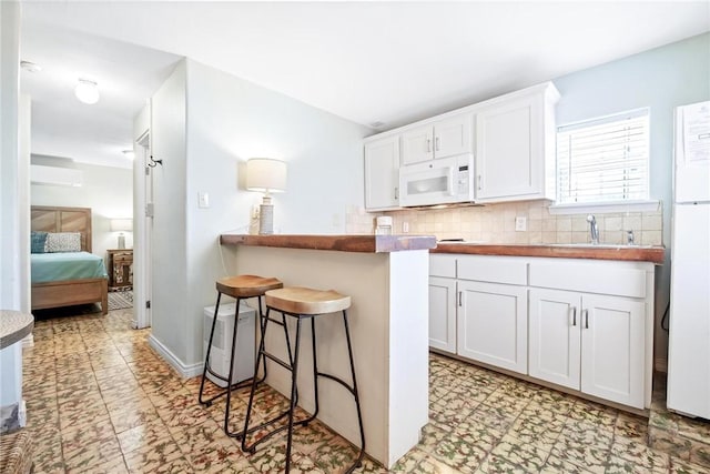kitchen with decorative backsplash, a kitchen bar, a sink, white microwave, and white cabinetry