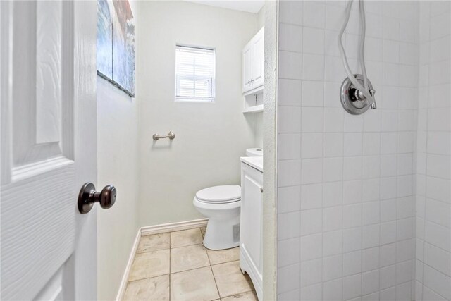 bathroom with a tile shower, vanity, toilet, tile patterned floors, and baseboards