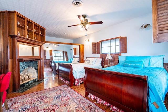 bedroom featuring light wood-type flooring, multiple windows, ceiling fan, and a high end fireplace