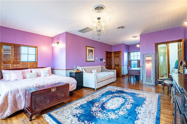 bedroom with a textured ceiling, wood-type flooring, multiple windows, and a notable chandelier