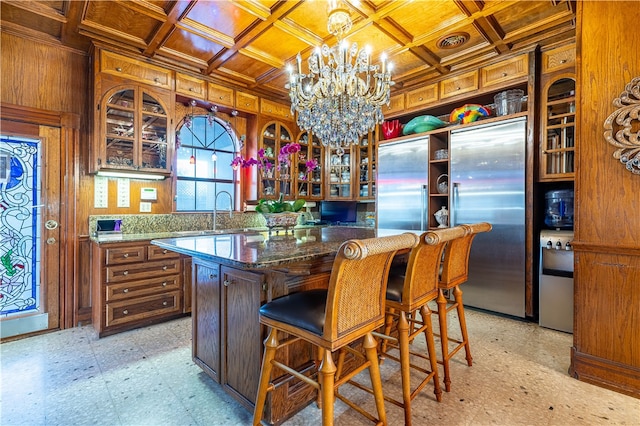 kitchen featuring wood walls, sink, built in refrigerator, coffered ceiling, and a center island