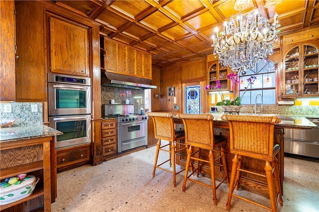 kitchen with stainless steel appliances, range hood, a notable chandelier, a kitchen bar, and sink