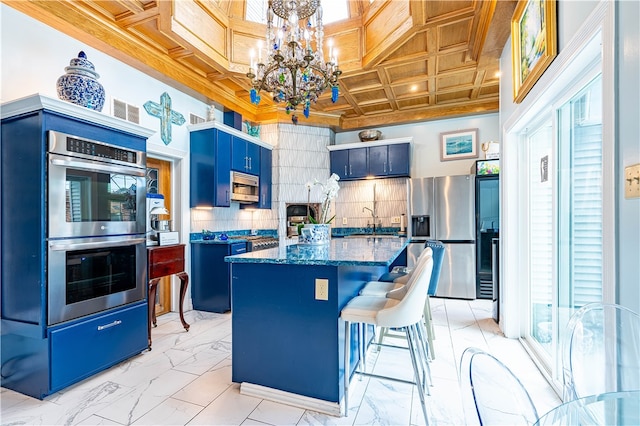 kitchen with stainless steel appliances, an inviting chandelier, a kitchen island, blue cabinets, and decorative backsplash