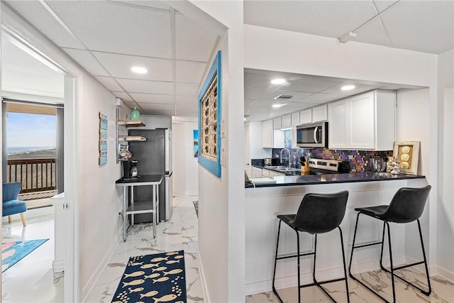 kitchen featuring stainless steel appliances, baseboards, decorative backsplash, marble finish floor, and white cabinets