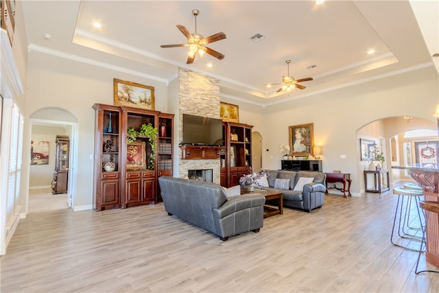 living room featuring a fireplace, a raised ceiling, ceiling fan, and light hardwood / wood-style flooring