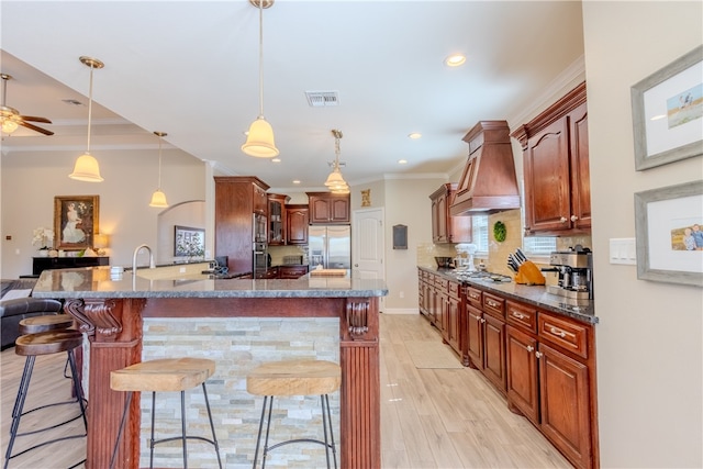 kitchen featuring a kitchen breakfast bar, appliances with stainless steel finishes, decorative light fixtures, and custom exhaust hood