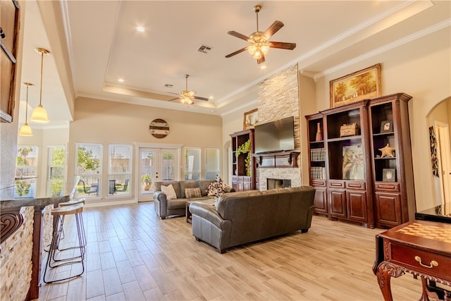 living room with a towering ceiling, ornamental molding, a raised ceiling, a fireplace, and light hardwood / wood-style flooring