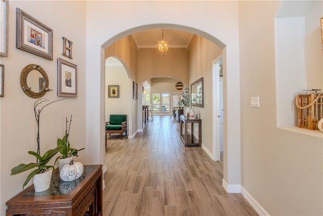 corridor featuring ornamental molding, light wood-type flooring, and a notable chandelier