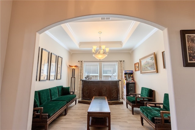 sitting room with an inviting chandelier, a raised ceiling, light hardwood / wood-style flooring, and crown molding