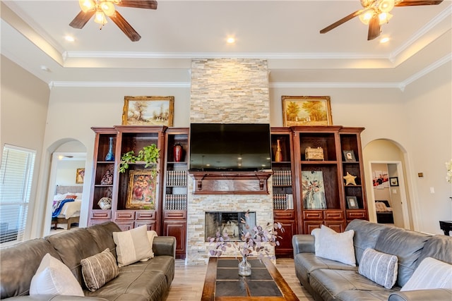 living room featuring a stone fireplace, light wood-type flooring, ceiling fan, and crown molding