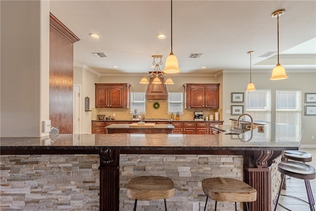 kitchen with a kitchen breakfast bar, decorative backsplash, hanging light fixtures, and crown molding