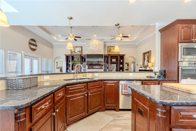 kitchen with sink, appliances with stainless steel finishes, dark stone countertops, a raised ceiling, and a kitchen island with sink