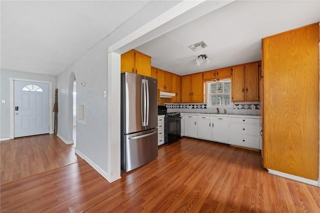 kitchen with sink, stainless steel fridge, light wood-type flooring, tasteful backsplash, and gas stove