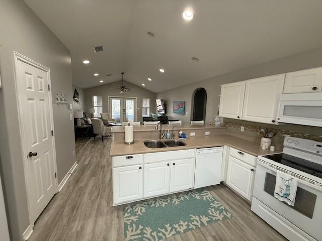 kitchen with a peninsula, white appliances, a sink, visible vents, and white cabinetry