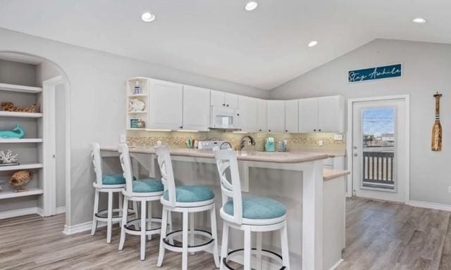 kitchen featuring a breakfast bar, white cabinets, lofted ceiling, and white microwave