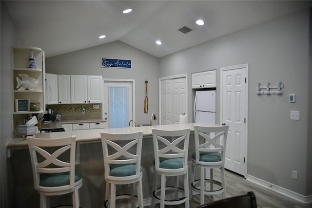 kitchen featuring lofted ceiling, visible vents, freestanding refrigerator, white cabinets, and a kitchen breakfast bar