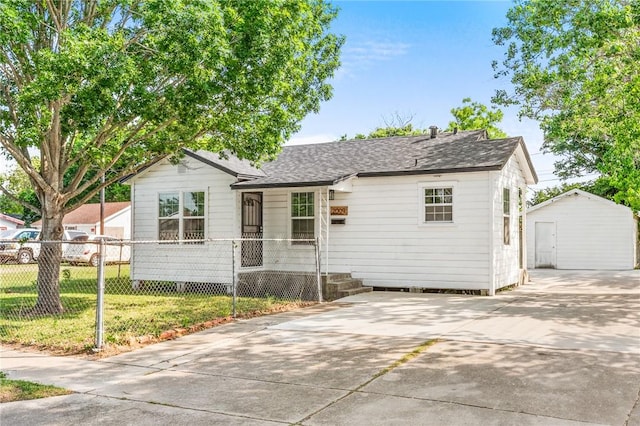 view of front of home featuring fence, roof with shingles, a front yard, an outbuilding, and concrete driveway