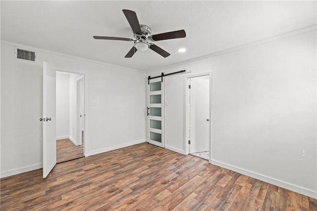 unfurnished bedroom with visible vents, wood finished floors, a barn door, ornamental molding, and recessed lighting