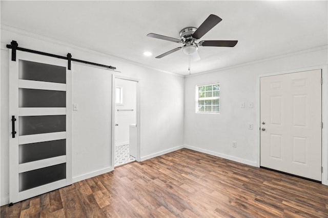 entryway with ornamental molding, wood finished floors, baseboards, ceiling fan, and a barn door