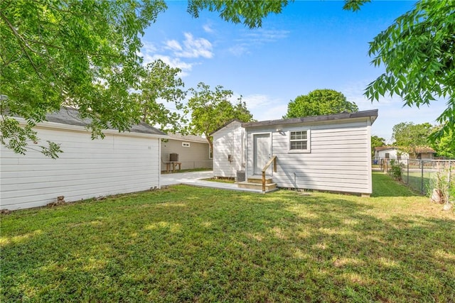 rear view of house with entry steps, fence, an outdoor structure, and a lawn