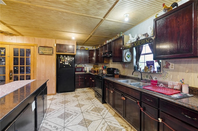 kitchen featuring dark brown cabinetry, black appliances, sink, and wooden walls