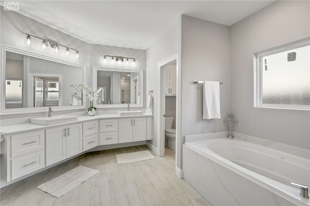 bathroom with a wealth of natural light, vanity, toilet, and tiled tub