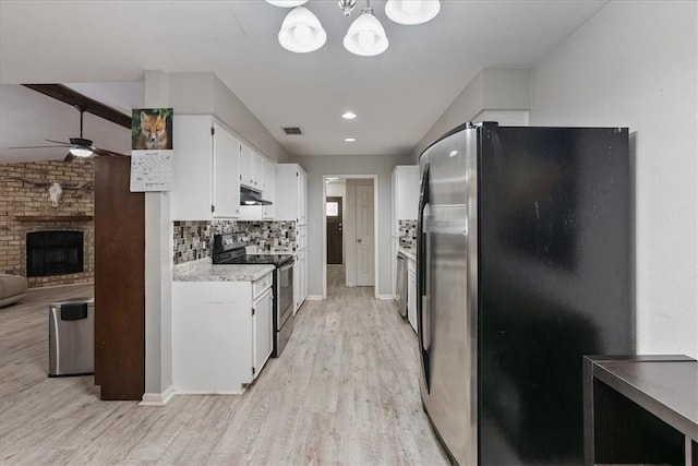 kitchen featuring visible vents, light wood-style flooring, a fireplace, appliances with stainless steel finishes, and backsplash