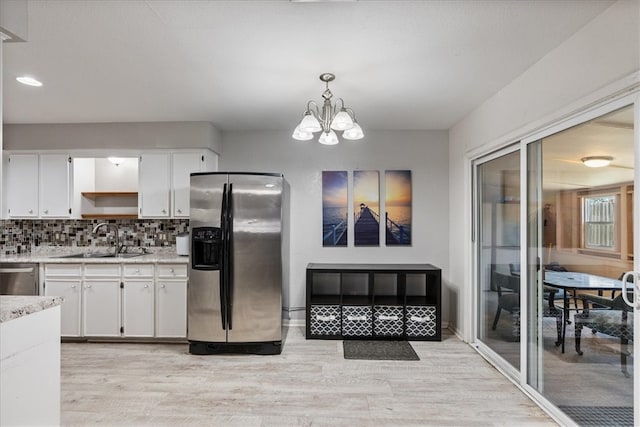 kitchen with a sink, white cabinets, light wood-style floors, appliances with stainless steel finishes, and tasteful backsplash