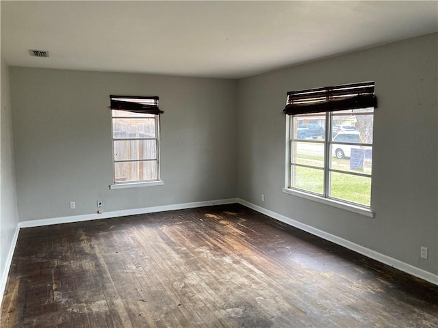 unfurnished room with visible vents, baseboards, and dark wood-style flooring