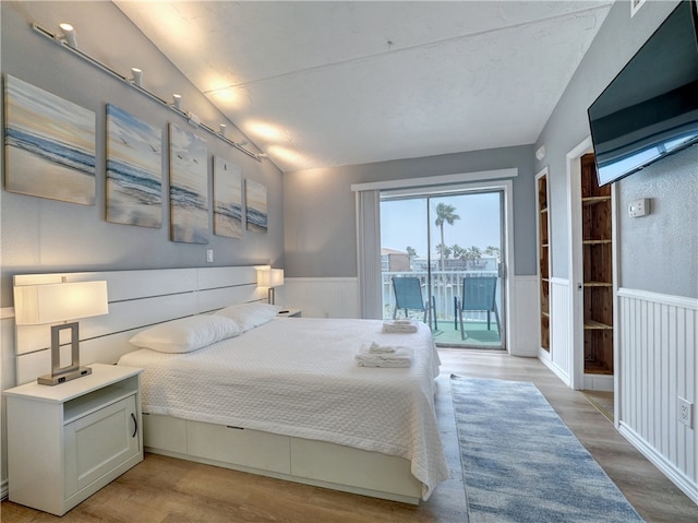 bedroom with lofted ceiling, access to exterior, and light hardwood / wood-style flooring