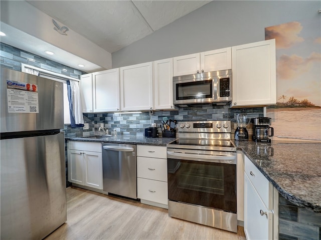 kitchen featuring stainless steel appliances, decorative backsplash, white cabinets, lofted ceiling, and light hardwood / wood-style flooring